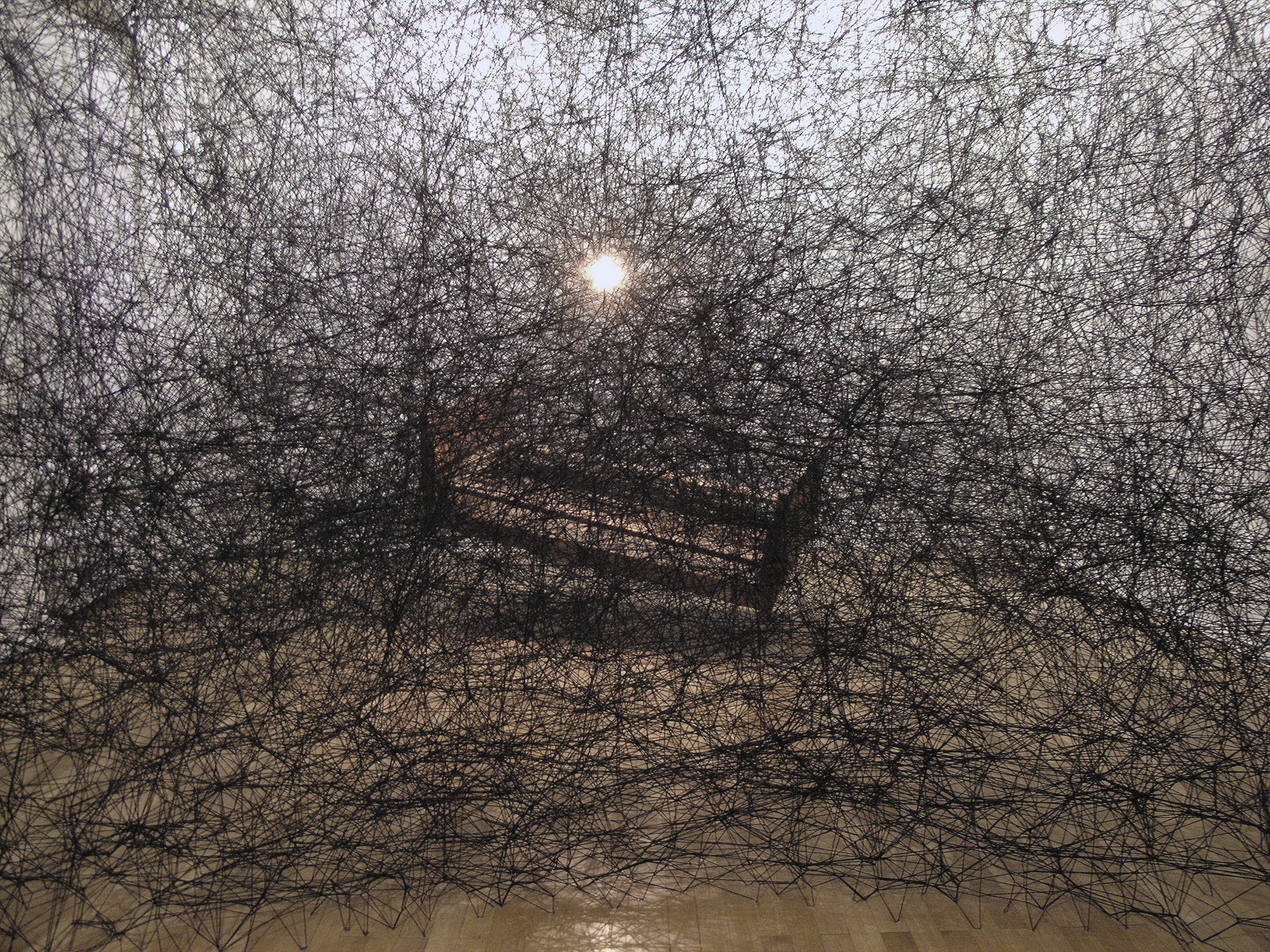 Chiharu Shiota During Sleep, 2005 Installation: wooden bed frame, light bulb, black wool Haus am Lützowplatz, Berlin, Germany Photo by Sunhi Mang ©︎ 2021 VG Bild-Kunst, Bonn, and Chiharu Shiota